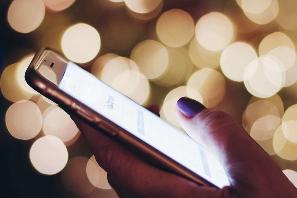vrouw scrollt met duim op mobiele telefoon met een achtergrond van geblurde lichtjes